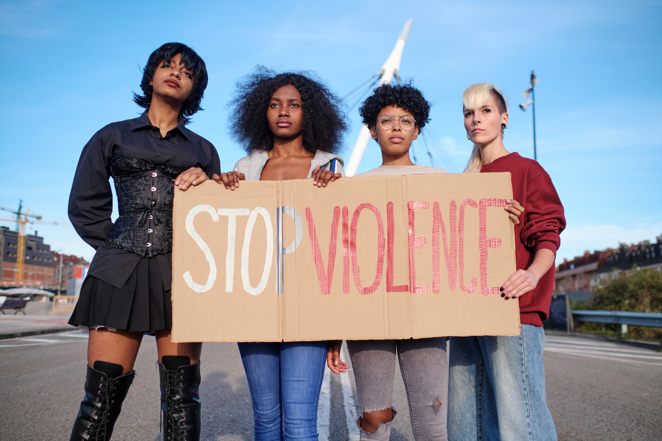 Four multi-ethnic women holding a large placard protesting against gender violence.